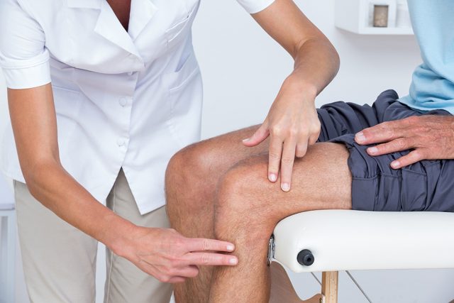 Doctor examining her patient knee in medical office